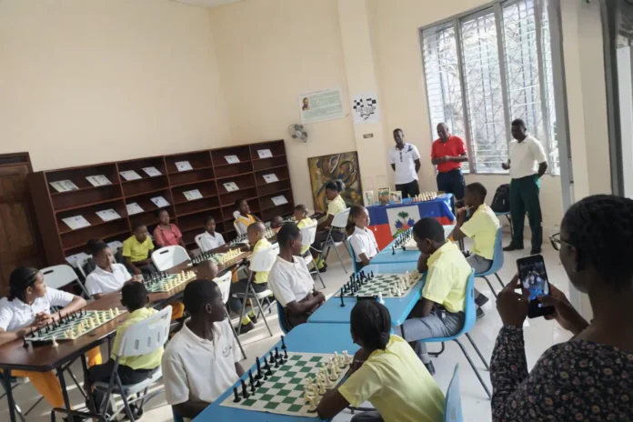 Photo d’un tournoi de jeu d’échecs à Jacmel, où des élèves haïtiens participent à une activité éducative dans une salle de classe lumineuse.